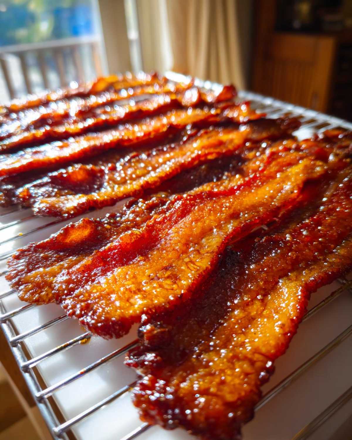 Several strips of glistening Brown Sugar Glazed Bacon resting on a wire cooling rack, fresh from the oven.