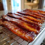 Several strips of glistening Brown Sugar Glazed Bacon resting on a wire cooling rack.