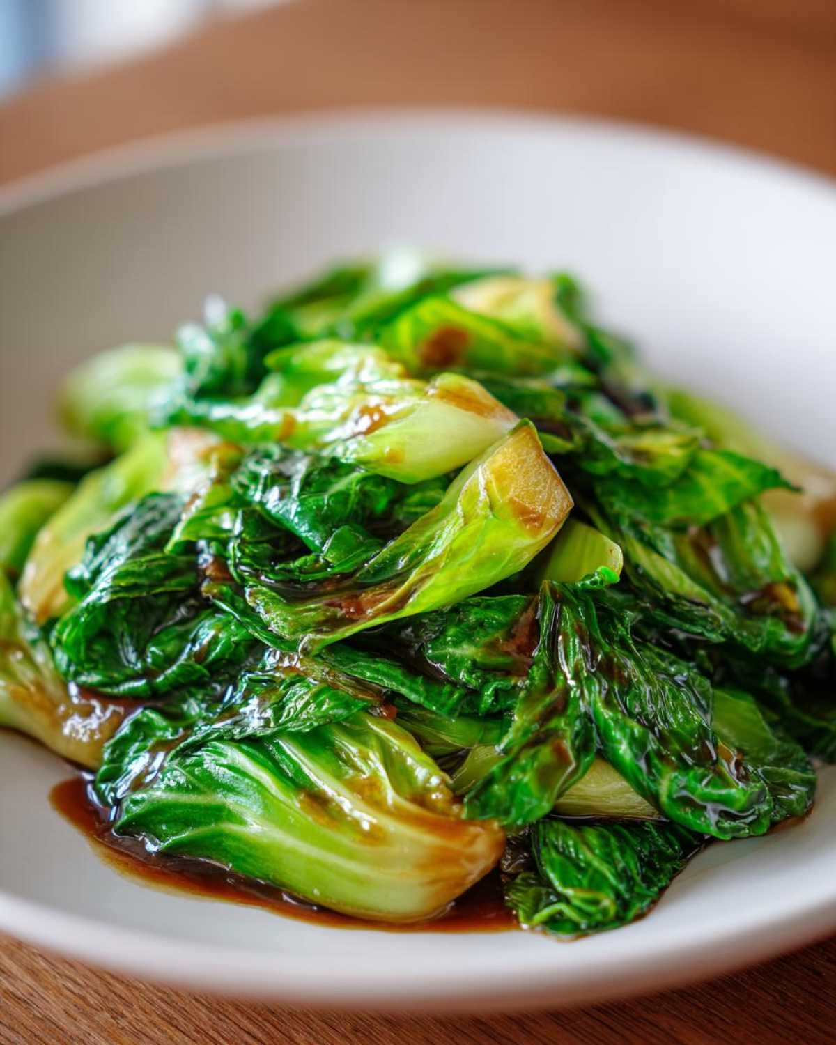 Close-up of vibrant green cabbage stir fry coated in a glossy garlic ginger sauce, served on a white plate.