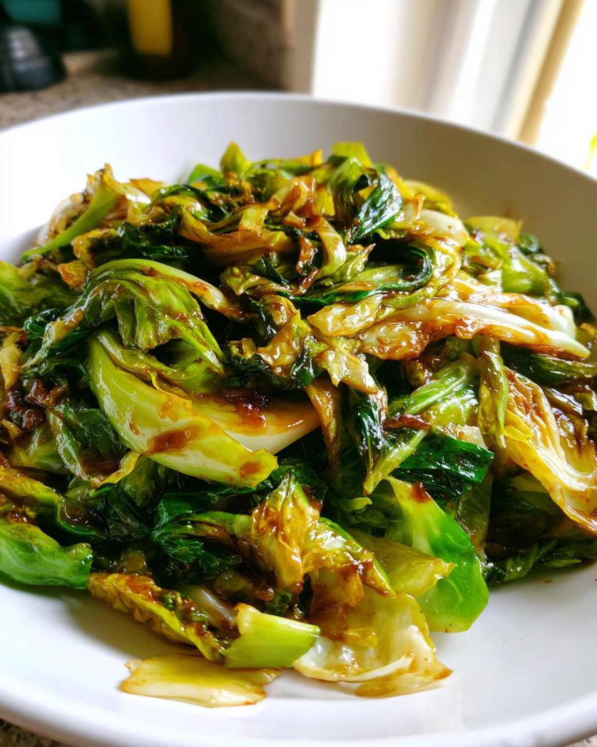 A close-up view of vibrant green and slightly caramelized cabbage stir fry coated in a rich garlic ginger sauce.