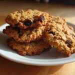 A stack of four chewy Gluten-Free Oatmeal Raisin Cookies with visible oats and raisins on a white plate.