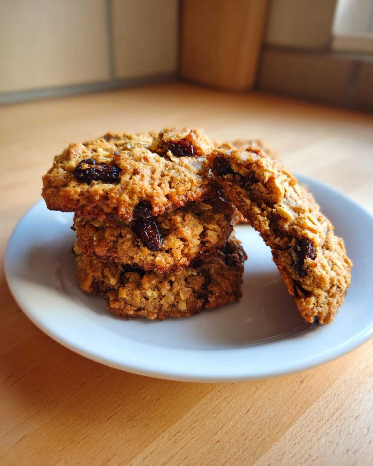 A stack of chewy Gluten-Free Oatmeal Raisin Cookies piled on a small white plate on a wooden surface.