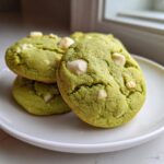 A stack of three chewy matcha white chocolate cookies with visible white chocolate chips on a white plate.