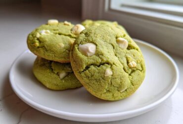 A stack of three chewy matcha white chocolate cookies with visible white chocolate chips on a white plate.