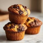 A stack of three freshly baked Chocolate Chip Banana Muffins with melted chocolate chips on top.