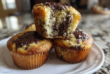 A stack of three moist Chocolate Chip Banana Muffins, one broken open to show the interior.