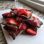 A stack of broken pieces of dark Chocolate Covered Strawberry Bark topped with fresh strawberry slices.