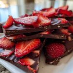 Stack of broken pieces of dark Chocolate Covered Strawberry Bark topped with fresh, sliced strawberries.
