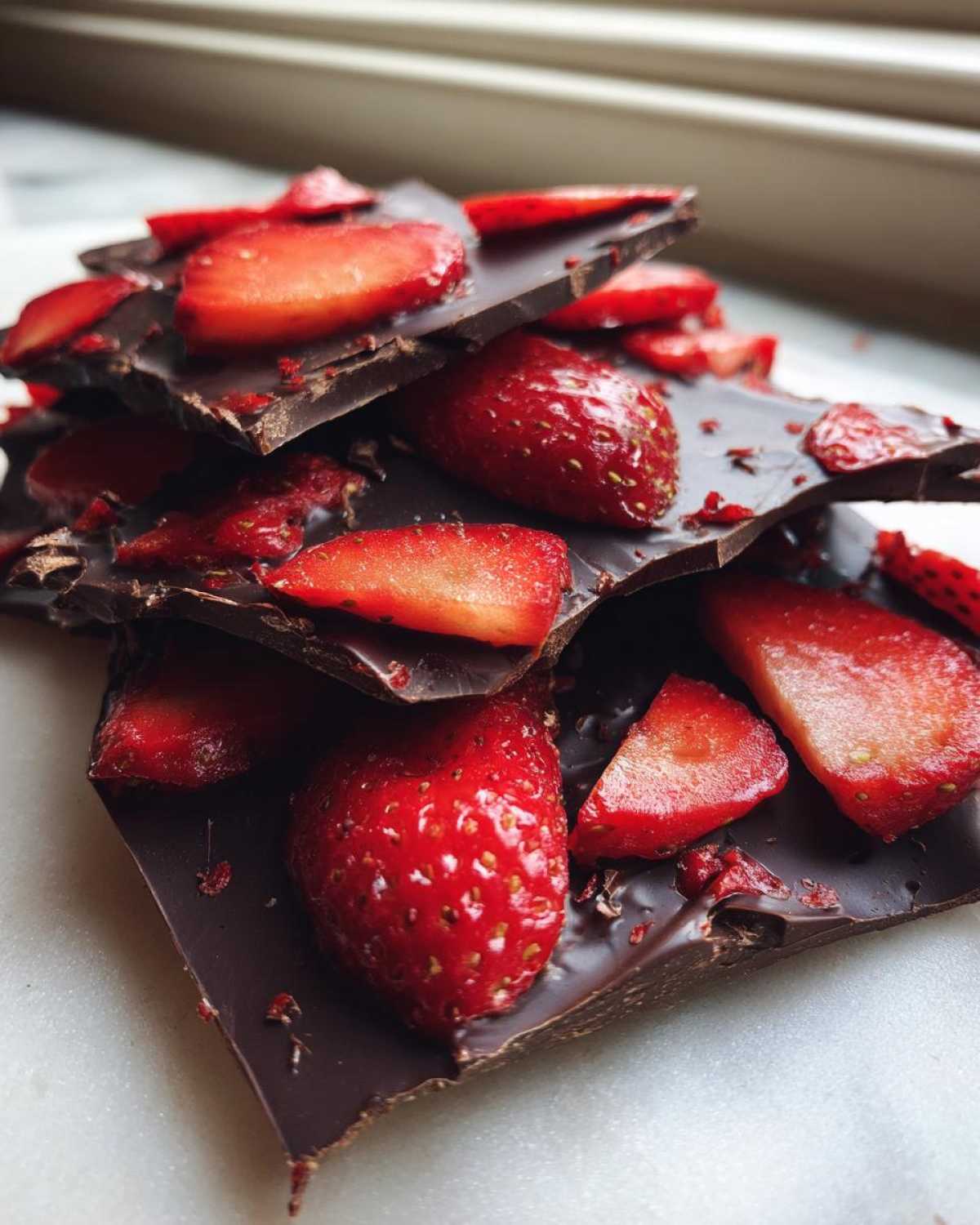 A close-up stack of dark Chocolate Covered Strawberry Bark pieces topped with fresh strawberry slices.