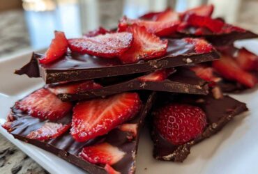 Stack of broken pieces of dark Chocolate Covered Strawberry Bark topped with fresh, sliced strawberries.