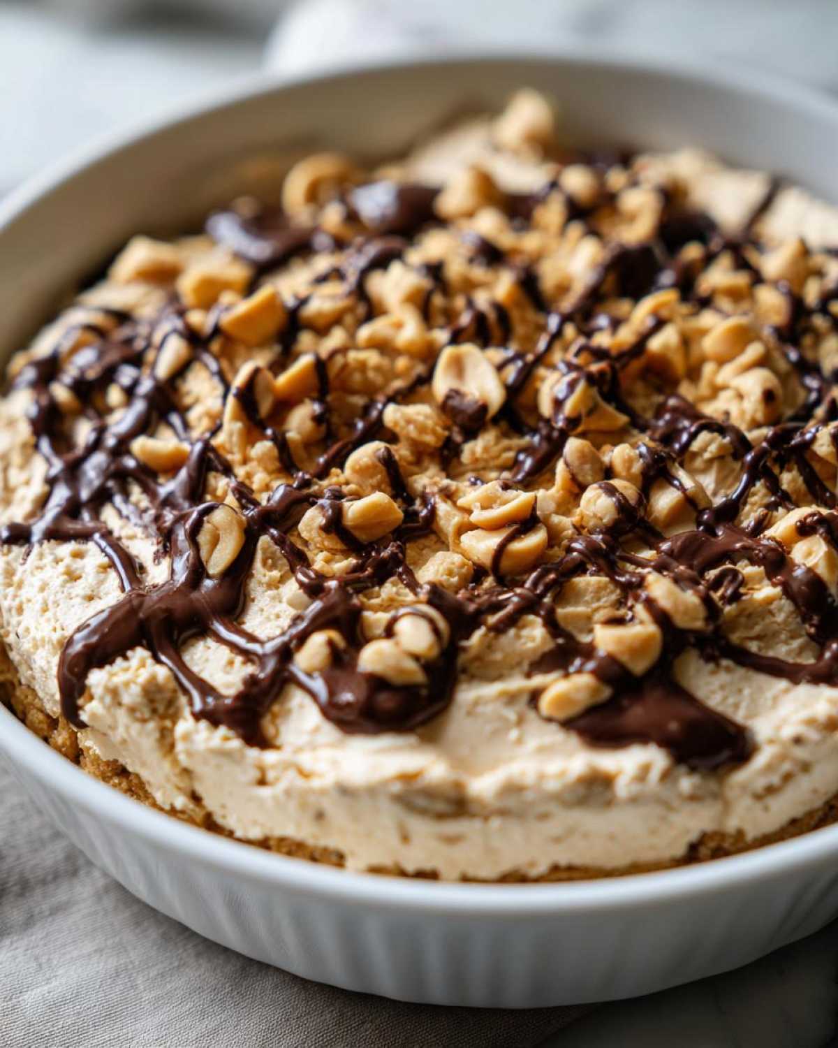 A close-up of the finished Chocolate Peanut Butter Cheesecake Dip topped with chopped peanuts and chocolate drizzle.