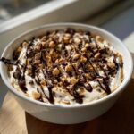 A white bowl filled with Chocolate Peanut Butter Cheesecake Dip, topped with whipped cream, chocolate drizzle, and peanut butter chips.
