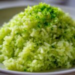 Close-up of bright green Cilantro Lime Rice mounded on a white plate, topped with fresh lime zest.