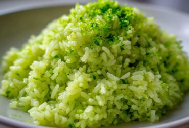 Close-up of bright green Cilantro Lime Rice mounded on a white plate, topped with fresh lime zest.