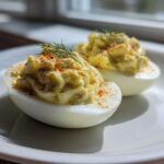 Two halves of Classic Deviled Eggs with Dill Pickle Relish, piped high and sprinkled with paprika and dill.