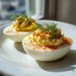 Two halves of Classic Deviled Eggs with Dill Pickle Relish, garnished with paprika and fresh dill, on a white plate.