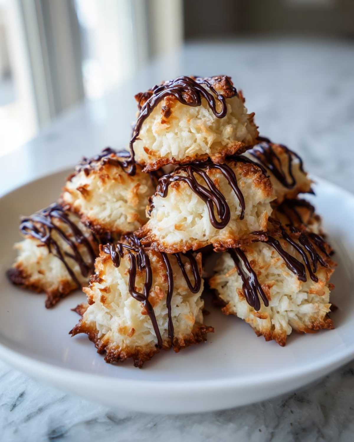 A stack of golden brown Coconut Macaroons with Dark Chocolate Drizzle piled on a white plate.