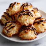 A stack of golden-brown Coconut Macaroons with Dark Chocolate Drizzle piled high on a white plate.