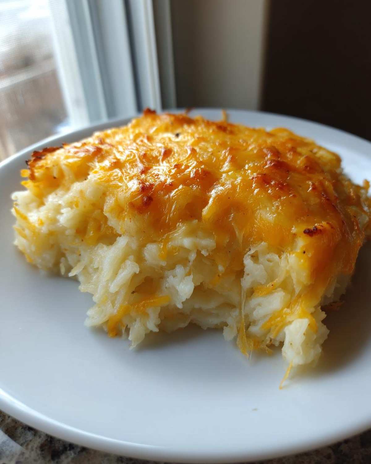 A close-up of a serving of Copycat Cracker Barrel Hashbrown Casserole with melted, golden cheese topping.