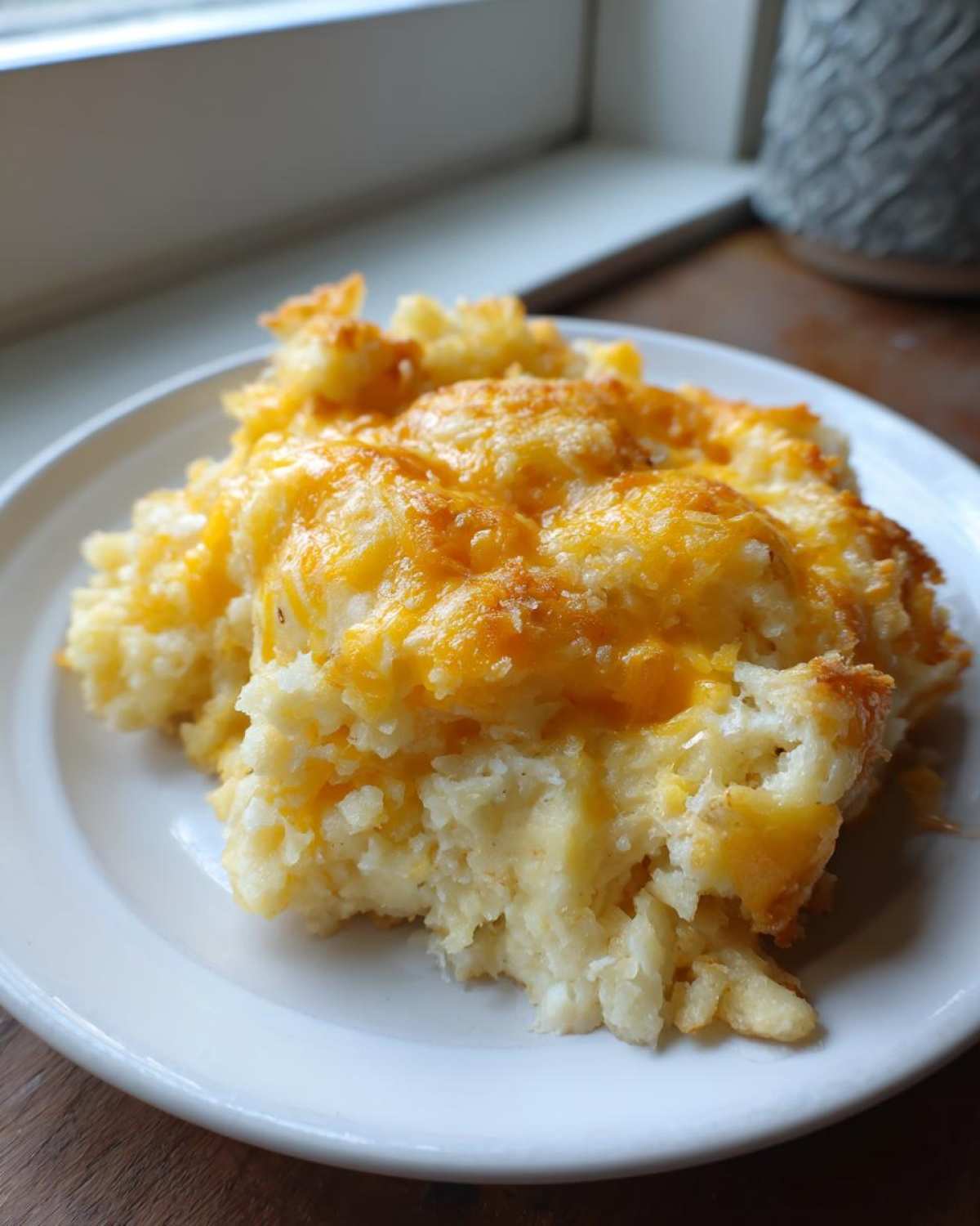 A generous serving of creamy Copycat Cracker Barrel Hashbrown Casserole topped with melted cheddar cheese on a white plate.