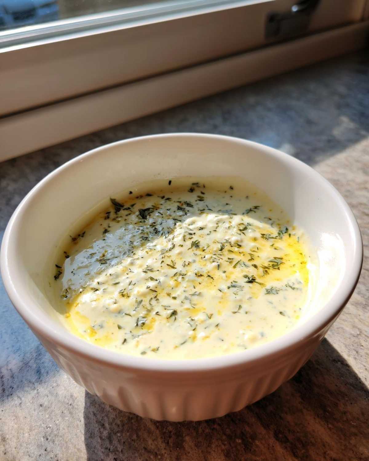 A white bowl filled with creamy Copycat Olive Garden Salad Dressing, topped with visible herbs and oil.