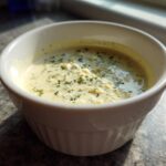 A white ramekin filled with creamy Copycat Olive Garden Salad Dressing, topped with green herbs.