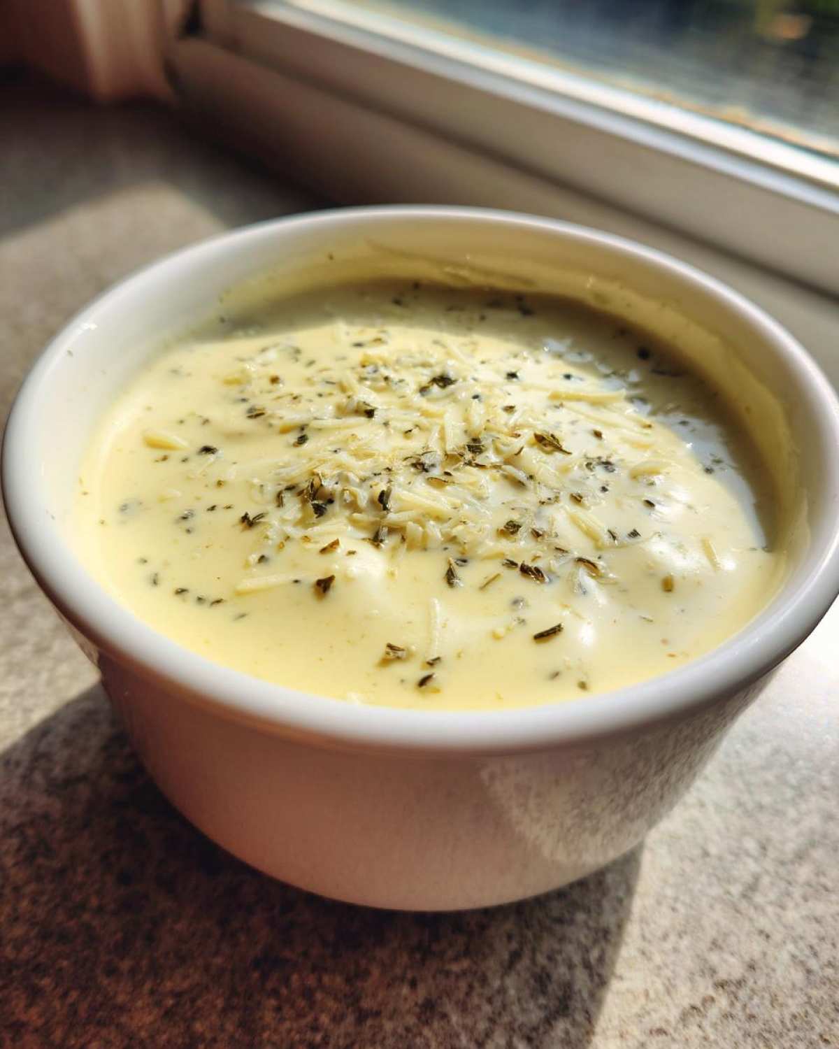 Close-up of creamy Copycat Olive Garden Salad Dressing topped with shredded cheese and dried herbs in a white bowl.