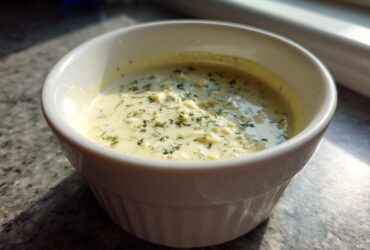 A white ramekin filled with creamy Copycat Olive Garden Salad Dressing, topped with green herbs.