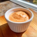 A close-up of creamy, orange-hued Copycat Raising Cane’s Sauce speckled with pepper in a white ramekin.