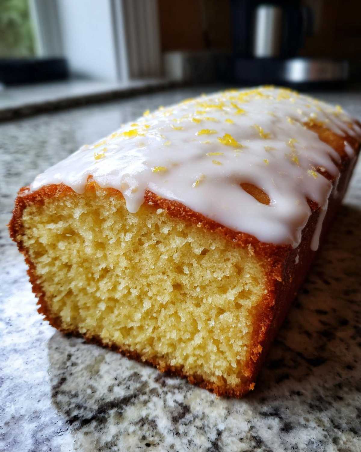 A close-up view of a freshly baked Copycat Starbucks Iced Lemon Loaf with white glaze and lemon zest.