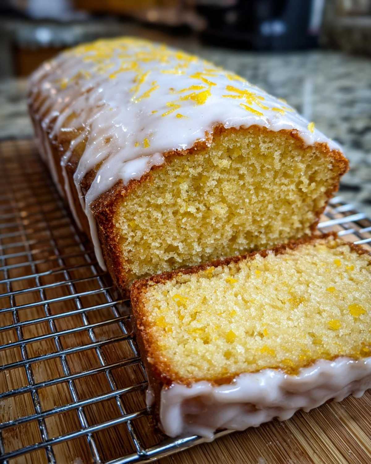 Close-up of a sliced Copycat Starbucks Iced Lemon Loaf with thick white glaze and yellow lemon zest.