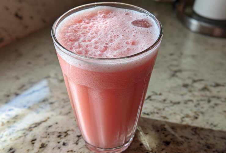 Close-up of a tall glass filled with the bright pink liquid of a Copycat Starbucks Pink Drink, showing foam on top.