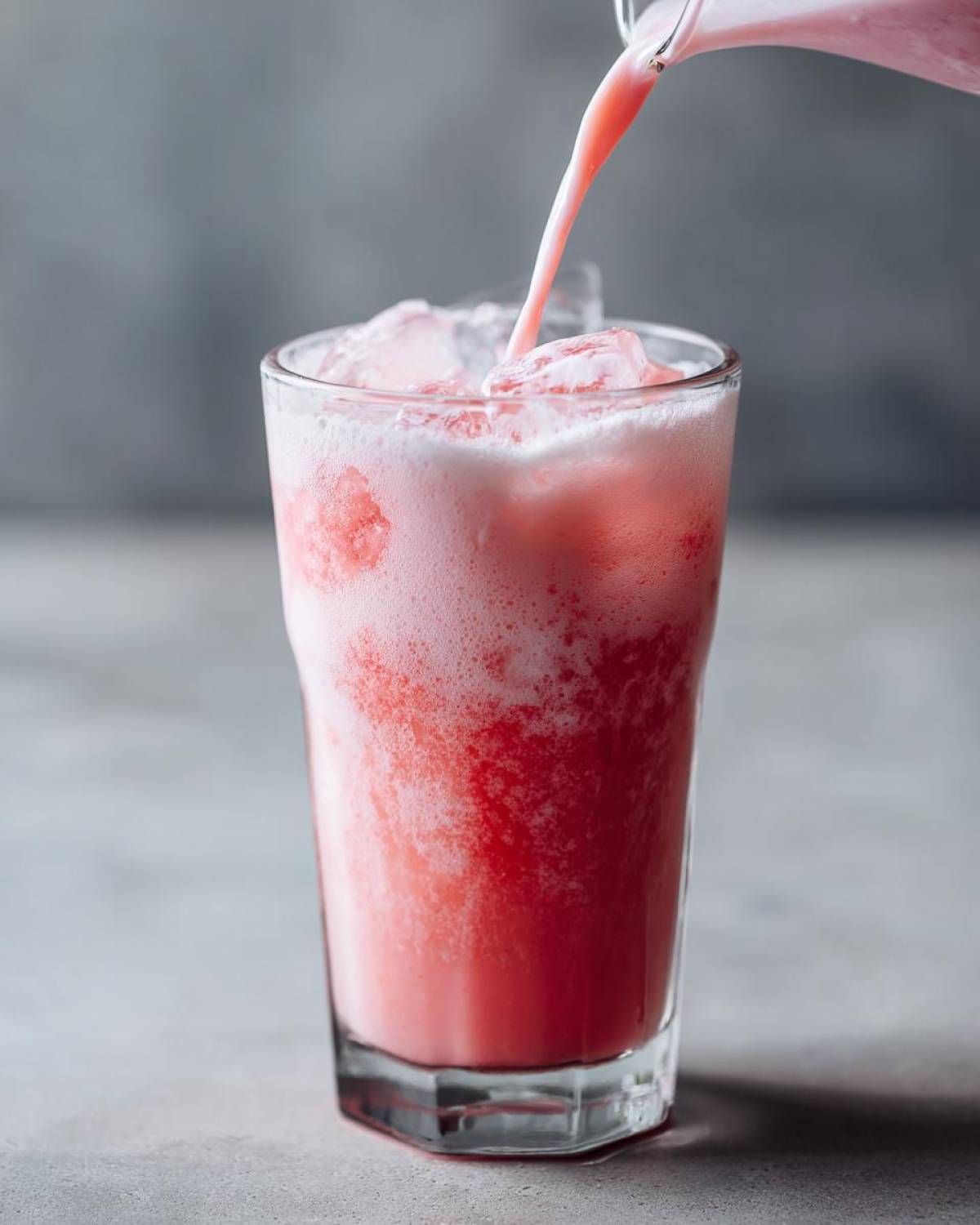 A stream of pink liquid is poured into a glass filled with ice to make a Copycat Starbucks Pink Drink.