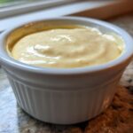 Close-up of creamy, yellow Copycat Taco Bell Chicken Quesadilla Sauce served in a small white ramekin.