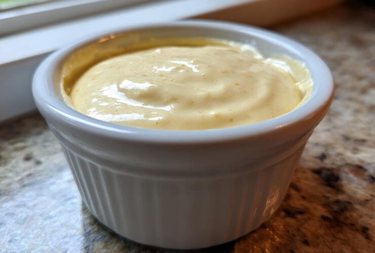 Close-up of creamy, yellow Copycat Taco Bell Chicken Quesadilla Sauce served in a small white ramekin.