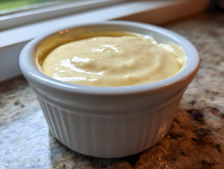 Close-up of creamy, yellow Copycat Taco Bell Chicken Quesadilla Sauce served in a small white ramekin.