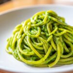 Close-up of bright green Creamy Avocado Pasta tossed in a rich sauce, served on a white dish.