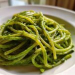 Close-up of bright green, saucy pasta noodles coated in Creamy Avocado Pasta sauce served on a white plate.