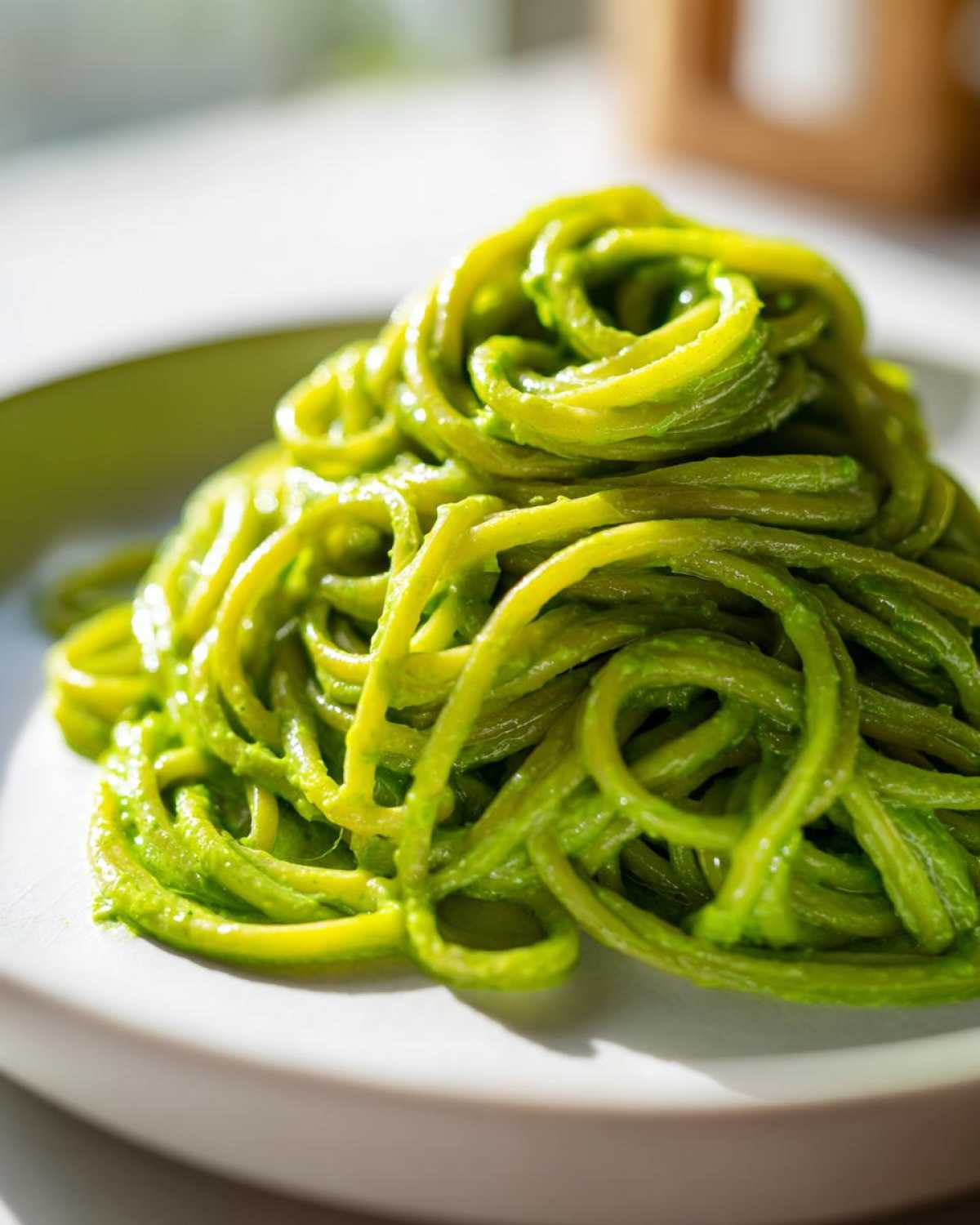 Close-up of bright green, glossy pasta coated in Creamy Avocado Pasta sauce, served on a white plate.