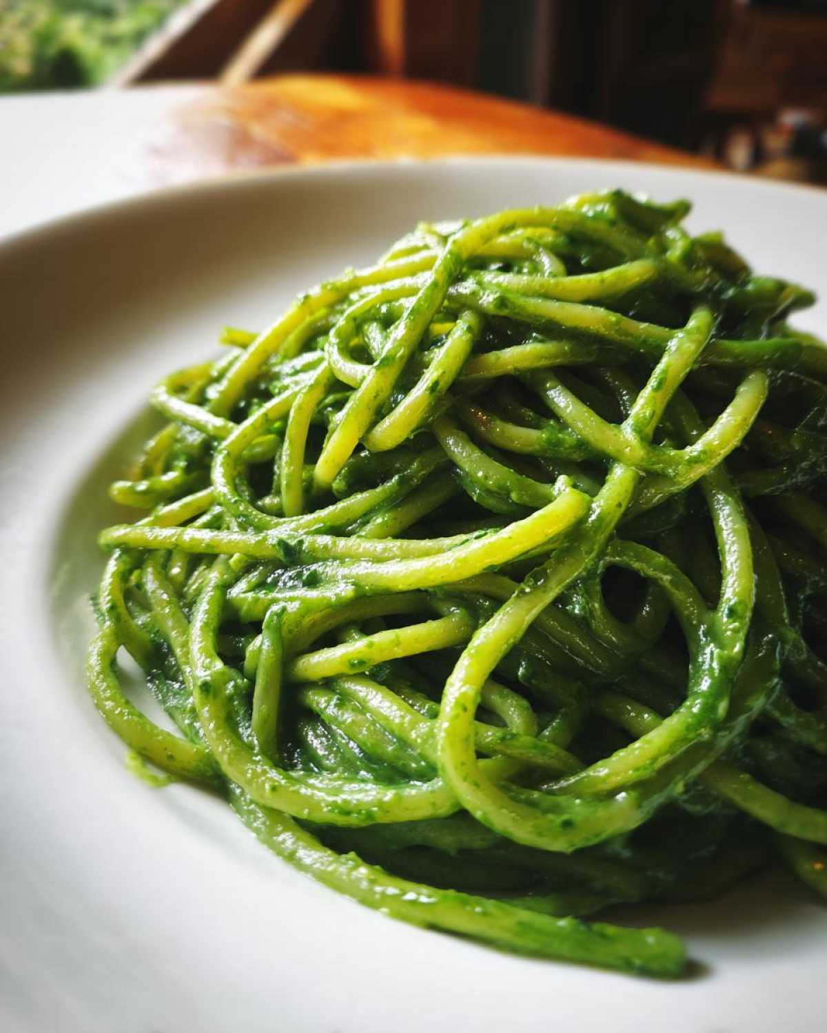 A close-up shot of spaghetti coated heavily in vibrant green, creamy avocado pasta sauce, served in a white bowl.