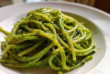 Close-up of bright green, saucy pasta noodles coated in Creamy Avocado Pasta sauce served on a white plate.