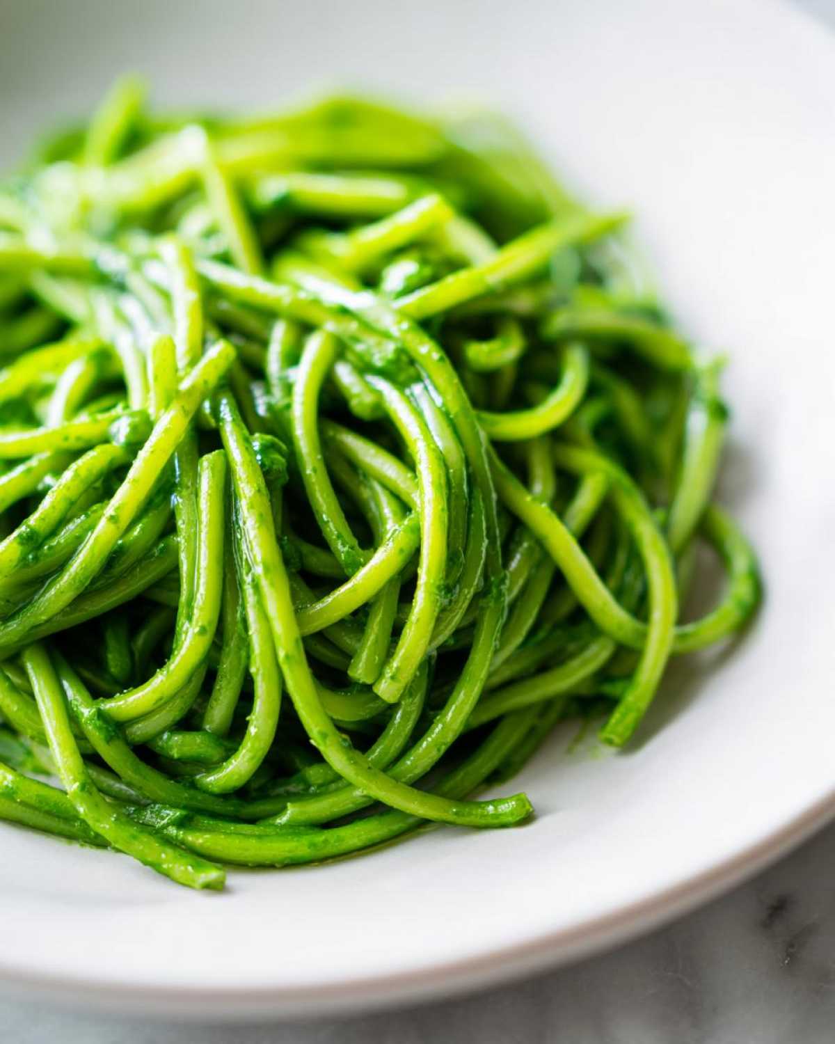 Close-up of vibrant green spaghetti coated in sauce, representing Creamy Avocado Pasta, served on a white plate.