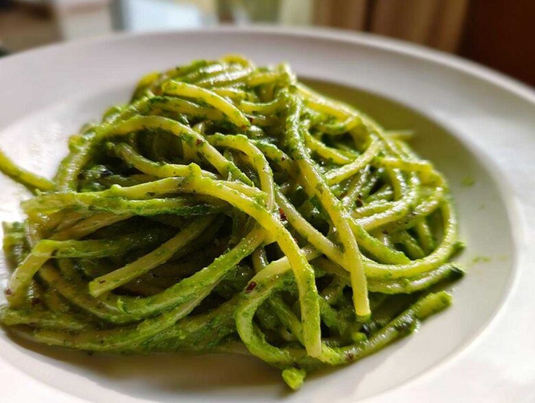 Close-up of bright green, saucy pasta noodles coated in Creamy Avocado Pasta sauce served on a white plate.
