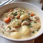 A close-up of a white bowl filled with rich Creamy Chicken Gnocchi Soup, featuring large gnocchi, shredded chicken, carrots, and parsley.