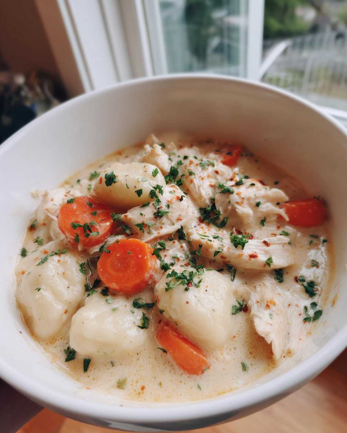 Close-up of a white bowl filled with Creamy Chicken Gnocchi Soup, featuring tender chicken, soft gnocchi, and sliced carrots.
