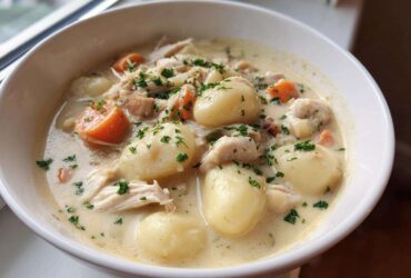 A close-up of a white bowl filled with rich Creamy Chicken Gnocchi Soup, featuring large gnocchi, shredded chicken, carrots, and parsley.
