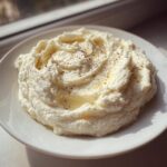 A mound of fluffy, white Creamy Garlic Mashed Cauliflower topped with melted butter and black pepper.