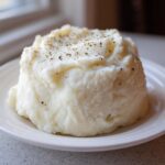 A mound of fluffy Creamy Garlic Mashed Cauliflower seasoned with pepper on a white plate.