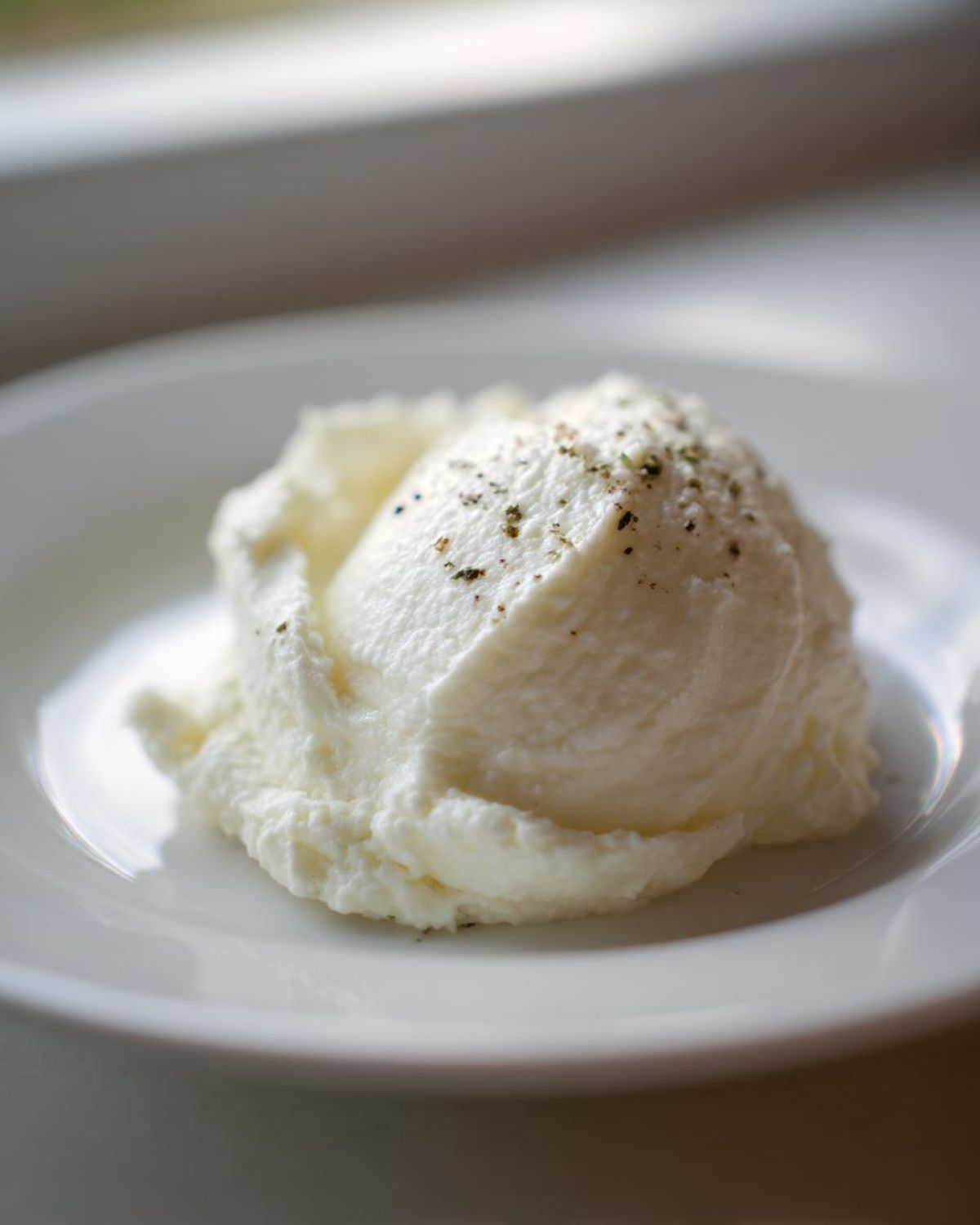A scoop of fluffy Creamy Garlic Mashed Cauliflower topped with cracked pepper and herbs on a white plate.