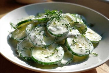 Close-up of sliced cucumbers coated in a white, creamy dressing and topped with fresh dill, showcasing Creamy German Cucumber Salad.